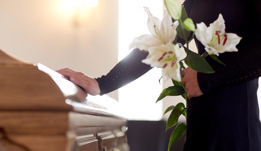 this image shows a mourner holding white flowers next to a coffin.