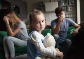 a family sitting in a living room. the child looks sad and the parents are not speaking to each other.